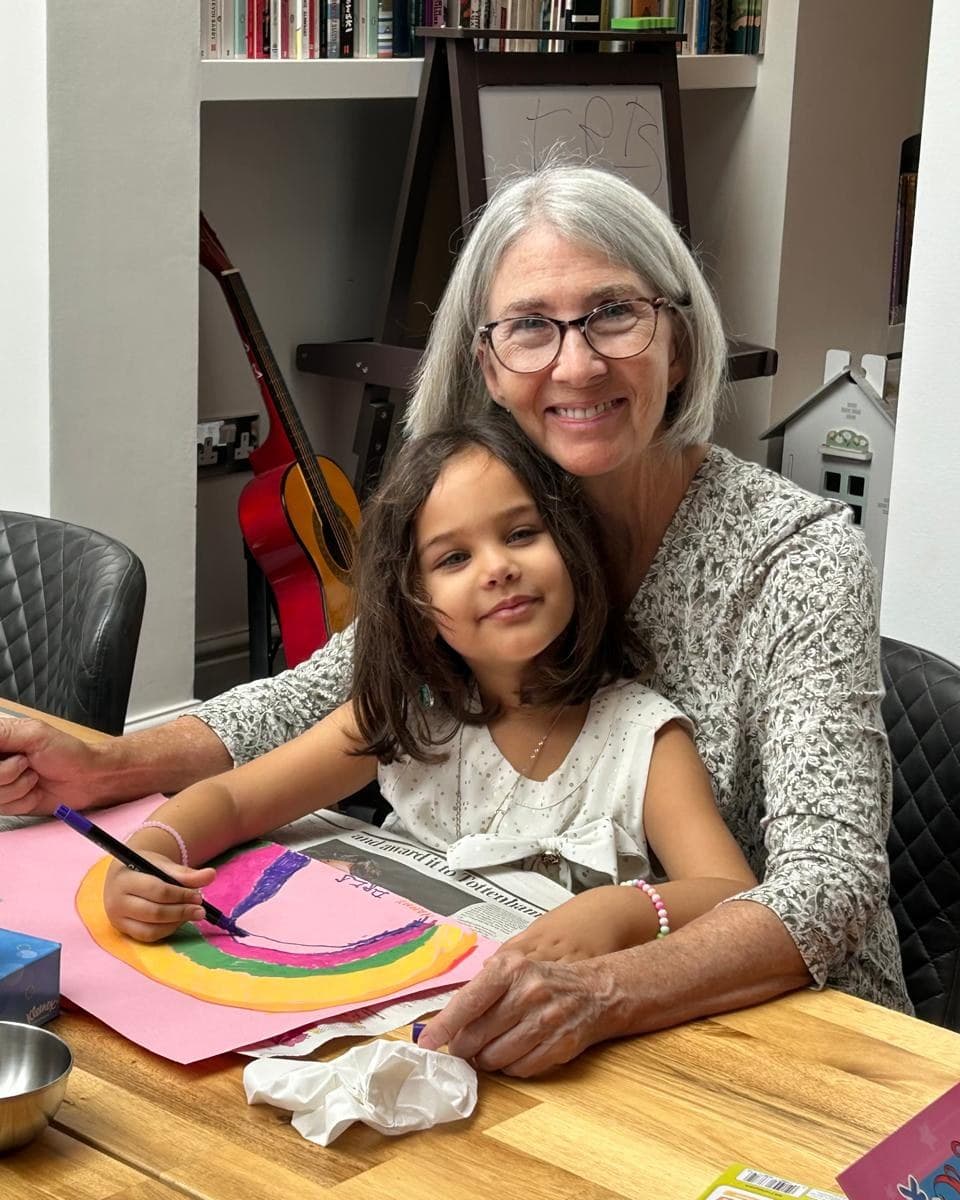 Karen Gregory at a table with her granddaughter, who is drawing a rainbow